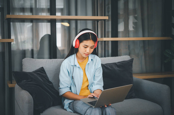 young student wearing headphones studies online,conversation via video call,distance learning on the sofa in the house - Photo, Image