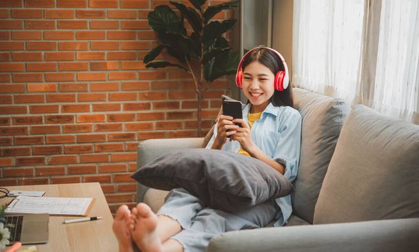 mujer adolescente con auriculares se sienta en su teléfono mientras escucha música, juega juegos, ordena en línea en el sofá cómodamente en un café. - Foto, imagen