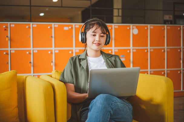 mujer adolescente con auriculares se sienta en su teléfono mientras escucha música, juega juegos, ordena en línea en el sofá cómodamente en un café. - Foto, imagen