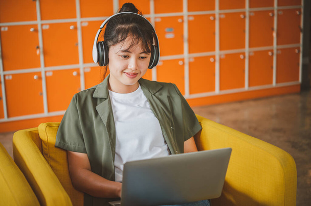 mujer adolescente con auriculares se sienta en su teléfono mientras escucha música, juega juegos, ordena en línea en el sofá cómodamente en un café. - Foto, Imagen