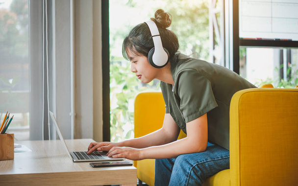 dospívající žena nosí sluchátka sedí na telefonu při poslechu hudby, hraní her, objednávání online na pohovce pohodlně v kavárně. - Fotografie, Obrázek