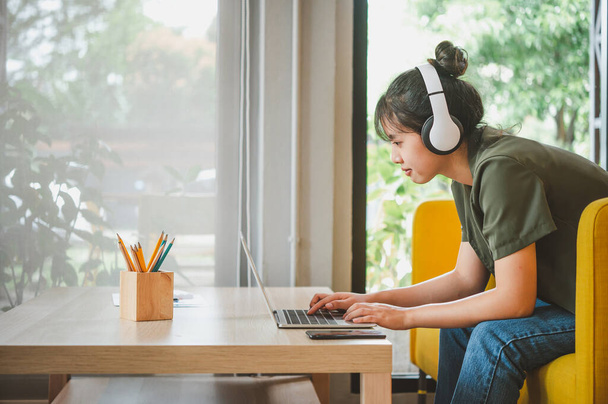 dospívající žena nosí sluchátka sedí na telefonu při poslechu hudby, hraní her, objednávání online na pohovce pohodlně v kavárně. - Fotografie, Obrázek