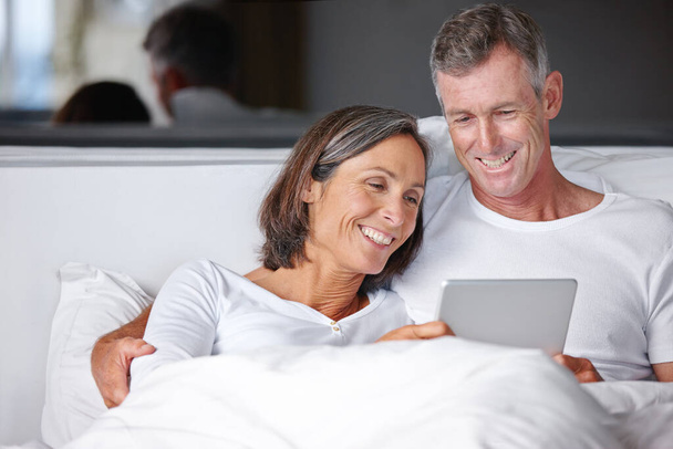 Zábava v posteli. šťastný dospělý pár sedí v posteli s digitálním tabletem - Fotografie, Obrázek