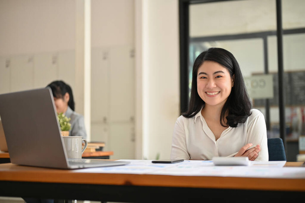 Attrayant et heureux jeune femme d'affaires asiatique ou gestionnaire financier féminin assis à son bureau bureau dans la salle de co-working de bureau. - Photo, image