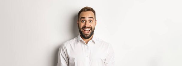 Close-up of caucasian bearded man looking excited, standing amazed against white background. - Foto, Imagem