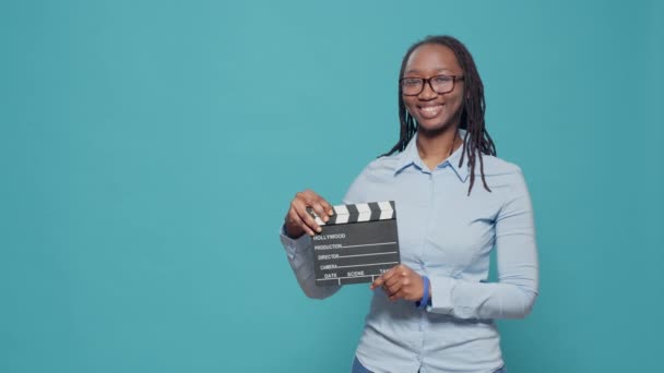 Portrait of african american woman holding film slate board used in movie and cinematography industry. Using action clapperboard as filmmaker or producer in filmography production. - Кадры, видео