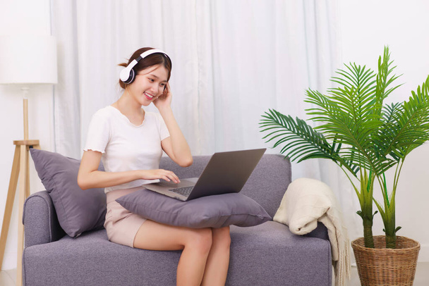 Lifestyle in living room concept, Young Asian woman in headphone to watching movie on laptop. - Foto, Imagen