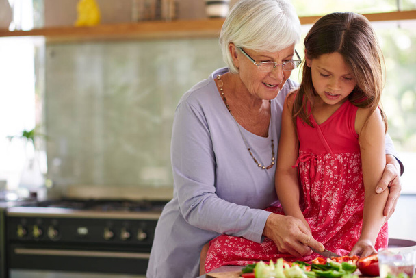 Однажды ты станешь отличным поваром. маленькая девочка помогает бабушке готовить обед - Фото, изображение