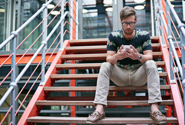 Průběžně informuje své klienty. pohledný mladý muž pomocí svého mobilního telefonu, zatímco sedí na schodech kanceláře - Fotografie, Obrázek