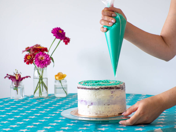 Woman spreading the icing to cover the top of the cake. Home baking, handmade. Free time on quarantine. Confectioner hands topping a cake with mint filling using a pastry bag. Selective focus. - Photo, image
