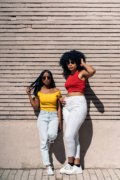 Confident african american girls posing and looking at camera against brown wall in the city. - 写真・画像