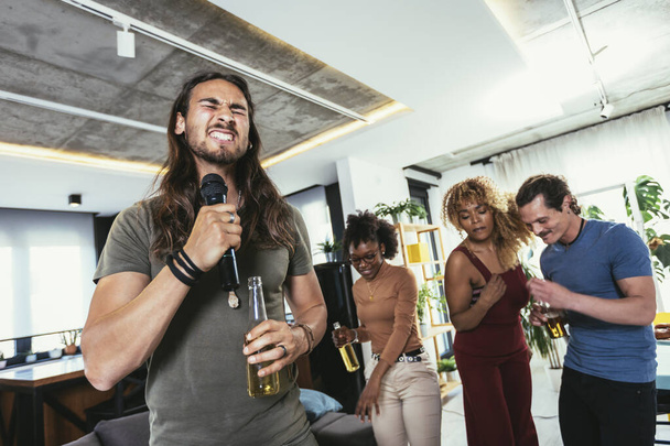 Grupo de jóvenes amigos multiculturales que hacen fiesta cantando canciones usando micrófono en casa. - Foto, imagen