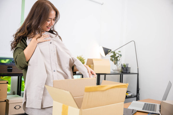 Happy Asian woman customer opening box and shirt against body new clothes, Excited smiling female shopper unboxing cardboard box package, shopping online from home, delivery shipping concept - 写真・画像