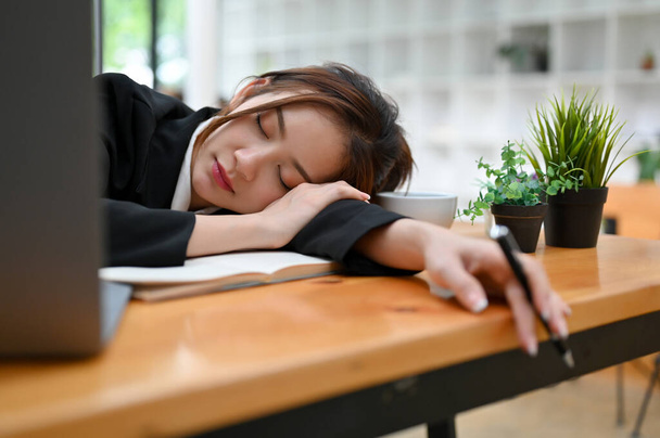 Νυσταγμένη και κουρασμένη νεαρή Ασιάτισσα επιχειρηματίας ή γυναίκα offie εργαζόμενη που κοιμάται ή κοιμάται στο γραφείο της. - Φωτογραφία, εικόνα