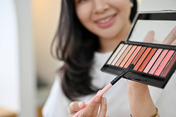Linda milenar asiática blogueira beleza feminina revisando uma paleta de sombra de olhos para seus assinantes on-line, mostrando e revisando o produto. - Foto, Imagem