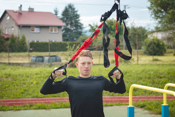 Professional athlete stretches and strengthens his arms, shoulders and pectoral muscles with trx fitness straps. Support training for maximum performance. Focused performance. - Photo, Image