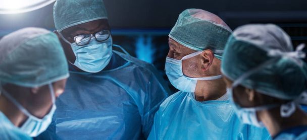 Diverse team of professional medical surgeons perform surgery in the operating room using high-tech equipment. Doctors work to save a patient in a modern hospital. The concept of medicine, technology - Photo, Image