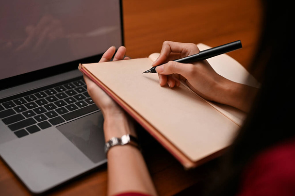 Uma bela mulher de negócios asiática escrevendo ou tomando notas algo em seu caderno em branco em sua mesa de escritório. corte tiro e close-up mãos imagem - Foto, Imagem