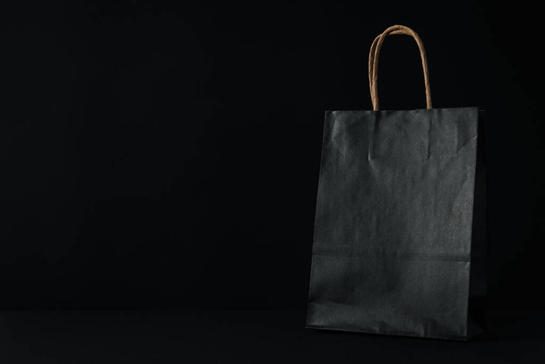 Black paper bag on black background, space for text - Фото, зображення