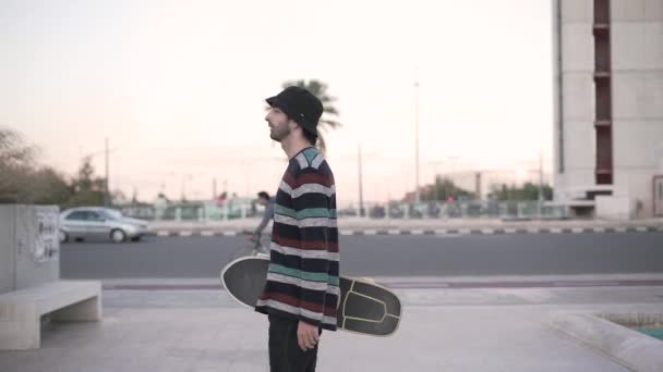Man draagt skateboard en loopt rond plein in de stad - 4K Horizontale video - Video
