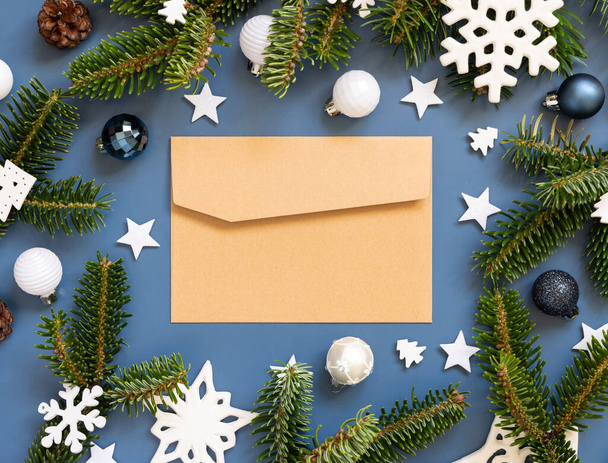 Käsityö paperi kirjekuori sinisellä taustalla lähellä valkoista joulukoristeita ja kuusen oksat ylhäältä näkymä, mockup, kopioi tilaa.. Uusi vuosi ja joululoma ilmakehän tasainen lay - Valokuva, kuva