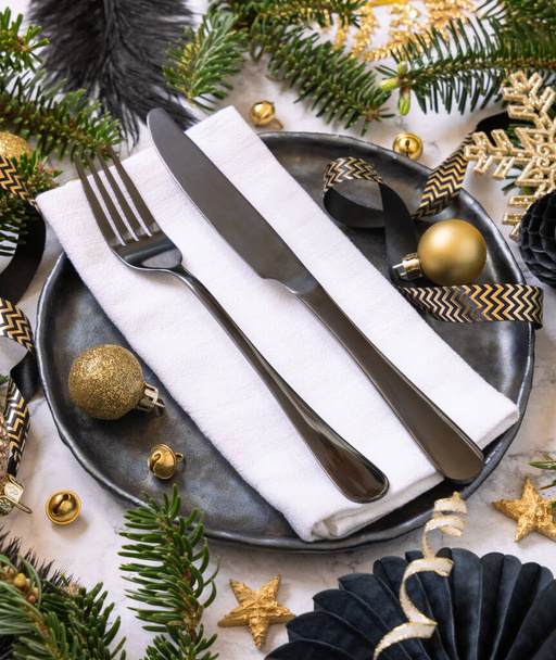 Black and golden Christmas table setting with decorations and fir tree branches close up. Winter table with fork, knife and plate. Winter New Year or Christmas dinner atmosphere - Фото, изображение