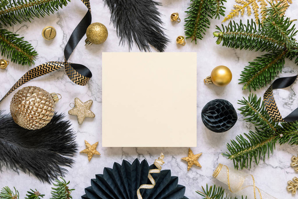 Čtvercová papírová karta mezi černými a zlatými vánočními ozdobami a jedlovými větvemi. Zimní kompozice s prázdnou pozvánkou Mockup, kopírovací prostor - Fotografie, Obrázek