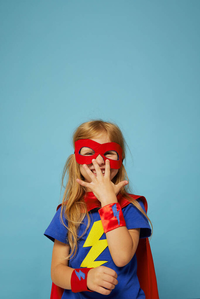 Funny little power super hero child (girl) in a red raincoat. Funny kid against blue background. Idea and creativity concept. - Foto, Imagem