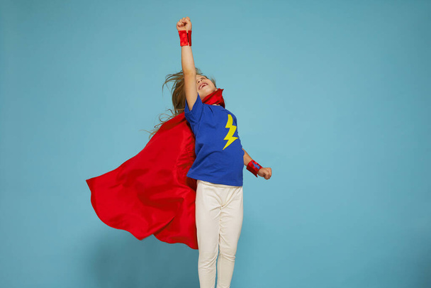 Funny little power super hero child (girl) in a red raincoat. Funny kid against blue background. Idea and creativity concept. - Фото, изображение