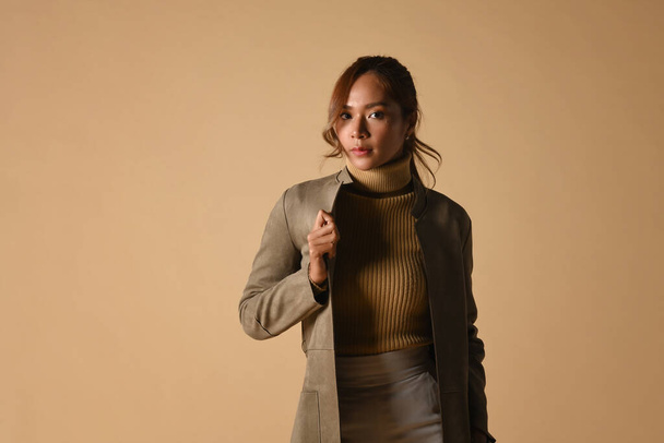 Portrait of beautiful woman in trench coat standing on beige background and looking at camera. Autumn fashion and beauty concept. - Valokuva, kuva