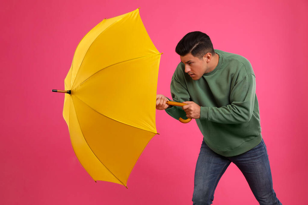 Emotional man with umbrella caught in gust of wind on pink background - Fotografie, Obrázek