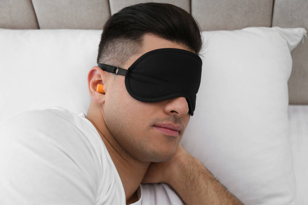 Man with foam ear plugs and mask sleeping in bed - Valokuva, kuva