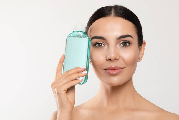 Young woman with micellar water on light grey background, space for text - Photo, Image