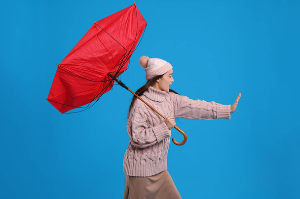 Young woman with umbrella caught in gust of wind on light blue background - Foto, Bild