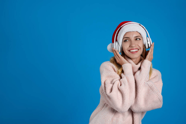 Happy woman with headphones on blue background, space for text. Christmas music - Foto, Imagen