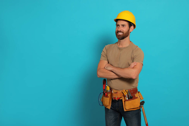 Professional builder in hard hat with tool belt on light blue background, space for text - Foto, Bild
