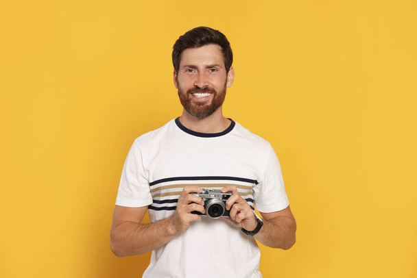 Man with camera on yellow background. Interesting hobby - Foto, imagen