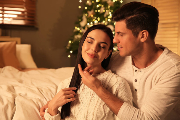 Ευτυχισμένο ζευγάρι σε εορταστικά διακοσμημένο υπνοδωμάτιο. Χριστουγεννιάτικη γιορτή - Φωτογραφία, εικόνα