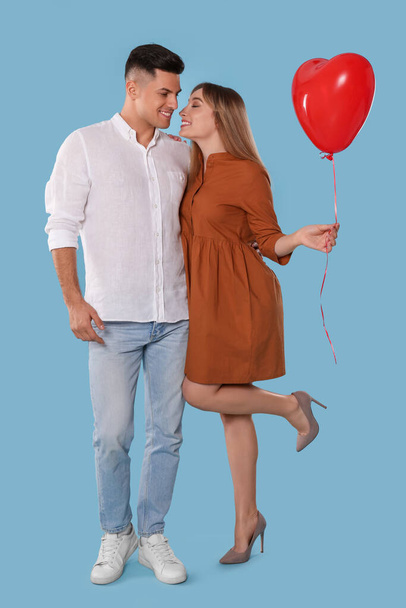 Lovely couple with heart shaped balloon on light blue background. Valentine's day celebration - Zdjęcie, obraz