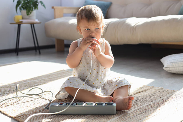 Baby girl playing with charger on floor at home. Dangerous situation - Foto, imagen