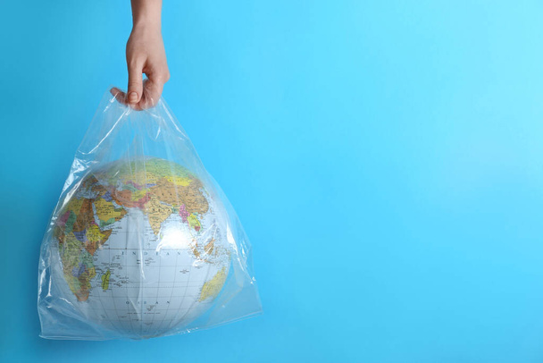 Woman holding plastic bag with globe and space for text on turquoise background, closeup. Environmental conservation - Foto, Bild