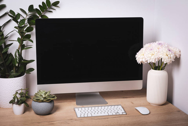 Comfortable workplace with modern computer, green houseplants and beautiful flowers on wooden table indoors - Foto, Imagen