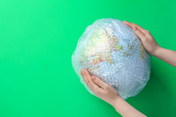 Woman holding globe packed in bubble wrap and space for text on light green background, top view. Environmental conservation - Φωτογραφία, εικόνα