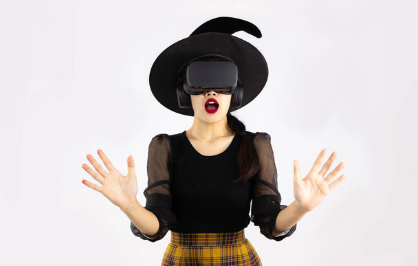 Young asian woman in halloween theme wearing vr goggles headset posing wow and surprised on white background. Metaverse concept. - Fotó, kép