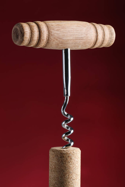 Corkscrew with cork against dark red background, closeup - Fotó, kép