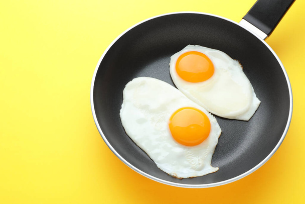 Tasty fried eggs in pan on yellow background, above view - Фото, изображение