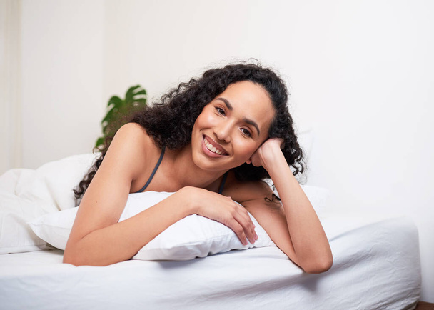Piękna młoda kobieta leży na brzuchu na poduszce w łóżku, uśmiechnięta i szczęśliwa. Wysokiej jakości zdjęcie - Zdjęcie, obraz