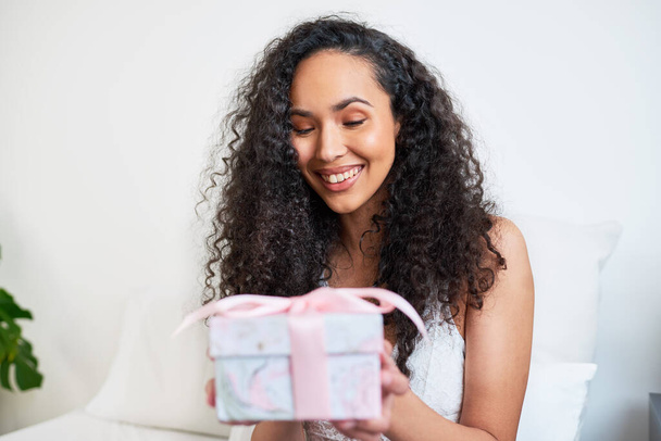 Een mooie jonge vrouw krijgt een cadeau in bed voor een speciale gelegenheid. Hoge kwaliteit foto - Foto, afbeelding
