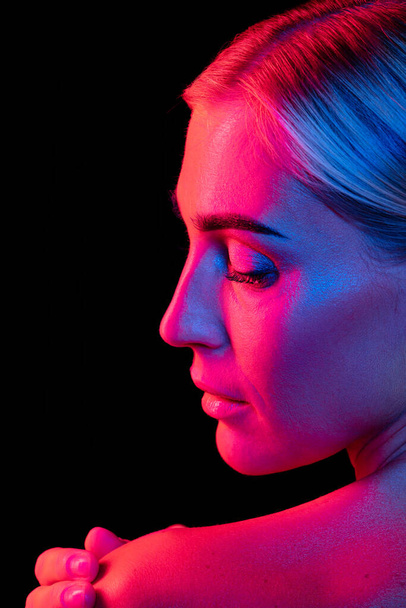 Nake shoulders and shiny perfect skin. Back view of young beautiful girl well-kept skin posing isolated over dark background in purple neon light. Fashion, beauty, health concept. - Fotoğraf, Görsel