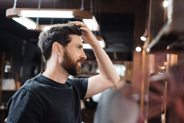side view of happy brunette man touching hair in barbershop - Foto, Imagen